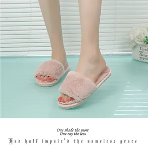 Close-up view of pink faux fur open toe house slippers worn by a model on a blue surface