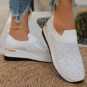 Vista detallada de zapatos de cuña blancos con pedrería brillante y detalles dorados.