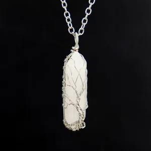 Close-up of wire-wrapped tree of life pendant on a white hexagonal crystal pillar.