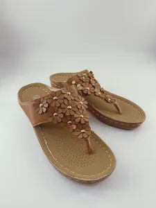 Vista dettagliata di sandali con zeppa marroni decorati con piccoli fiori in pelle e borchie.