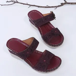 Detailed view of women's burgundy wedge sandals with floral accents and sparkling rhinestones
