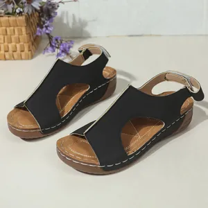 Detail van zwarte sleehak sandalen met witte contraststiksels en klittenbandsluiting.