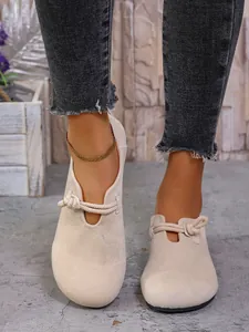 Detalle de zapatos planos de gamuza beige con punta redonda y lazo de cuerda decorativo