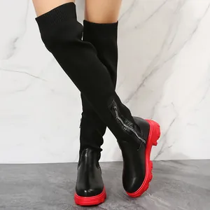 Detail of over-the-knee boots featuring black knit upper and bold red lug soles.