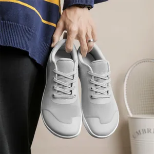 Pair of grey wide toe breathable barefoot shoes held by a hand in a home setting