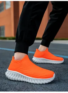 Close-up of bright orange fly-woven slip-on sneakers for men and women on an outdoor track.