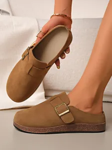 Close-up of brown suede closed-toe mules with adjustable buckle strap and cork sole.