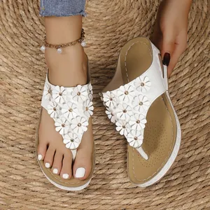 Dettaglio di sandali bianchi con zeppa decorati con fiori e borchie su tappeto di paglia naturale.