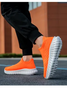 A detailed low angle view of vibrant orange fly-knit sock sneakers on asphalt ground