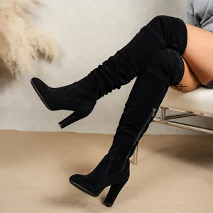 Close-up of black suede over-the-knee boots with high heels and ruched texture