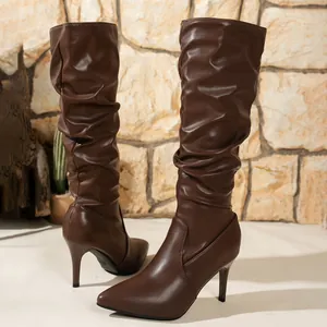 Botas altas marrones de tacón fino y punta afilada con un diseño de cuero fruncido.