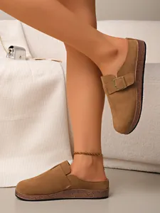 Detail shot of brown suede closed-toe mules featuring a stylish decorative metal buckle.
