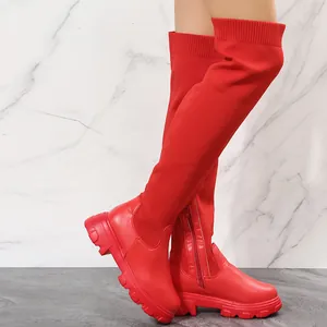 Detail shot of vibrant red over-the-knee boots featuring a chunky sole and knitted upper part.