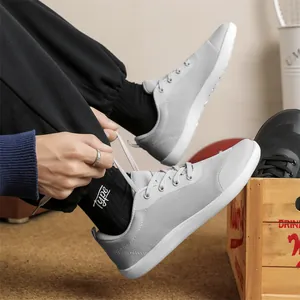 Side view of grey mesh barefoot sneaker being laced up by wearer in a casual setting