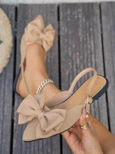 Detail van beige platte sandalen met spitse neus, een grote strik en getextureerde stof.
