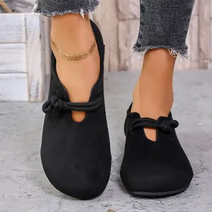 Vista detallada de mocasines planos de ante negro con un elegante detalle de nudo.