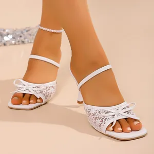 Close-up view of elegant white lace high heel sandals featuring bow detail and square toe