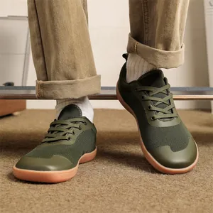 Close-up of green wide-toe barefoot sneakers worn with khaki pants on carpet.