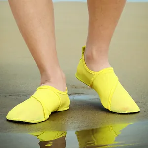 Detail of bright yellow mesh beach shoes worn on sand with a clear water reflection.
