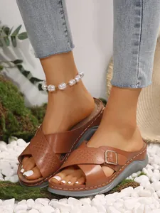 Detailed view of stylish brown cross-strap wedge sandals for women on natural pebbles