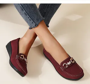Detailed view of burgundy suede loafers with decorative gold buckle and white stitching
