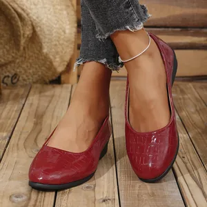 Detail view of red glossy crocodile embossed wedge shoes worn on a wooden floor