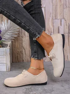 Primer plano de zapatos planos de ante beige para mujer con un detalle de nudo decorativo.