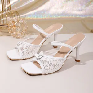 Detail view of white lace high-heeled mules with elegant rhinestone bow decoration