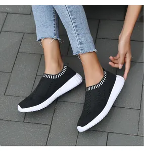 Side detail view of women's black breathable knit slip-on sneakers on stone pavement