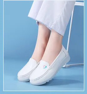Close-up detail of white nursing shoes with heart logo shown on a person's feet in blue studio