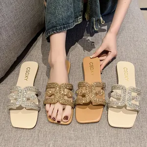 Macro view showing sparkling rhinestone H-strap details on flat sandals in tan and beige.
