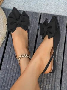 Detailopname van zwarte platte sandalen met spitse neus, grote strik en slingback-bandje.