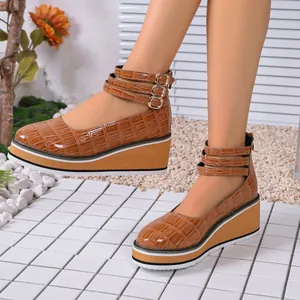 Détail des chaussures compensées en cuir verni marron à motif croco avec brides