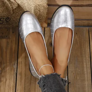 Close-up of silver crocodile-embossed women's flat shoes on wooden floor
