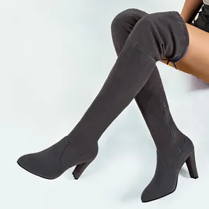 Gros plan sur des bottes cuissardes en daim gris foncé à talons hauts et au bout pointu.