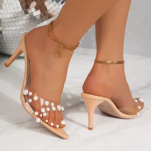 Close-up of elegant nude stiletto mules with transparent PVC strap and pearl accents
