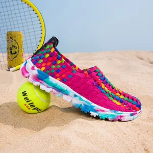 Detail view of colorful woven slip-on sneakers resting on a sandy beach with tennis balls.