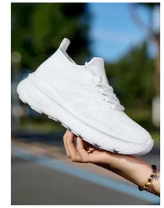 Detail view of a white breathable fly-knit sneaker with thick sole held by a person's hand