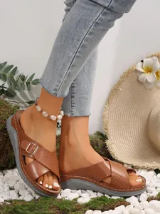 Detail view of brown wedge sandals with cross-straps and buckle on a beach-themed background