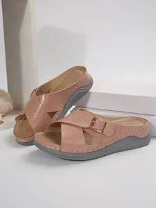 Detailed view of pink women's wedge slides featuring cross-straps and gold buckles