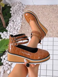 Détail de chaussures compensées en cuir verni marron à motif crocodile et trois brides