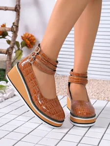 Vue détaillée d'escarpins compensés en cuir verni marron à motif croco et brides.