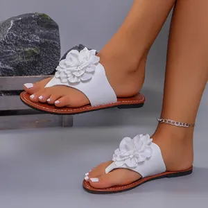 Vista detallada de chanclas planas con flores de tela blanca para mujer y suela marrón