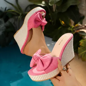 Pink suede wedge sandals with bow detail and woven jute sole in poolside setting