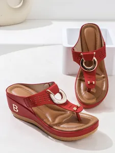 Detailed view of red wedge thong sandals featuring decorative gold circular hardware