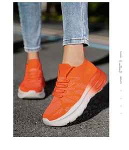 Close-up of bright orange fly-knit sports sneakers on model feet in outdoor setting.