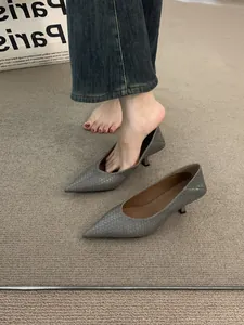 Detalle de zapatos de tacón bajo trenzados grises con punta fina sobre alfombra.
