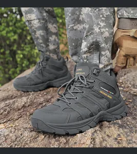 Close-up of grey mid-top tactical hiking boots on rocky terrain with camouflage pants