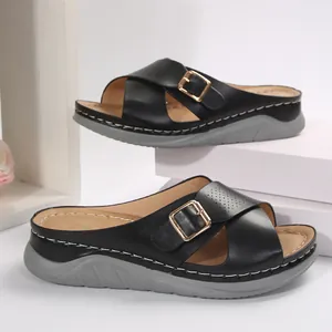 Detailed view of black women's platform slippers with cross straps and gold buckles.