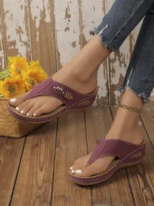 Detail of women's burgundy wedge thong sandals with hollow cutouts and gold accents.